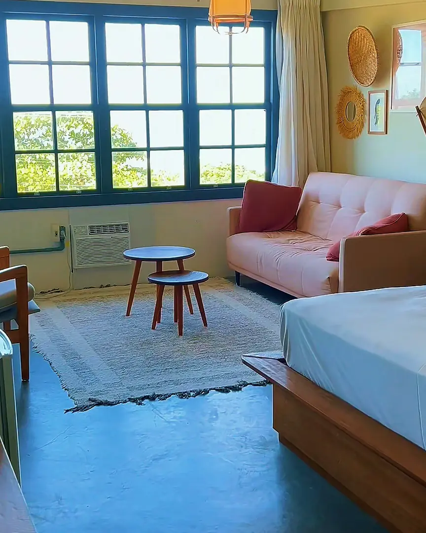 Quarto do complexo com cama de casal, sofá rosa e janelas grandes