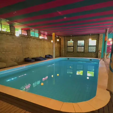 Piscina aquecida coberta, com teto listrado em rosa e verde e pufes na borda