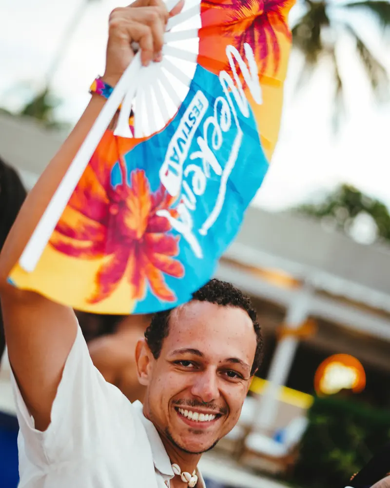Homem sorrindo com o leque oficial do Weekend Festival aberto no alto, na pool party