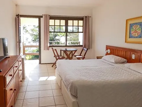 Quarto com cama de casal, mesinha e porta aberta para a varanda