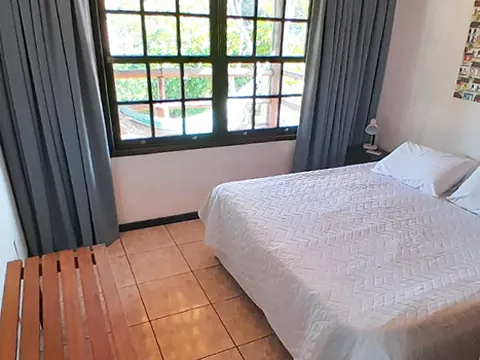 Quarto com cama de casal e janela de madeira com cortinas